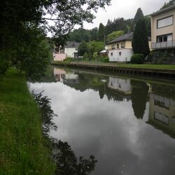 Foto: Ein begradigter Fluss mit Ufersicherung und einseitig mit Häusern, die bis auf wenige Meter an den Gewässerrand reichen.