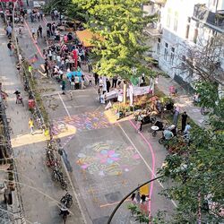 Straße aus der Vogelperspektive auf der Kinder spielen, Menschen spazieren und grüne Bäume zu sehen sind.