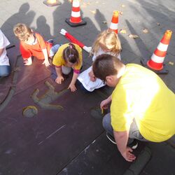 Kinder zeichnen die Umrisse des Verkehrsschilds auf den Boden