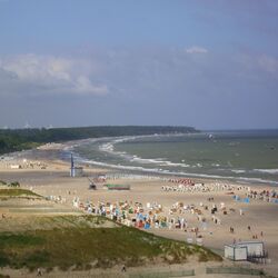 Blick auf Strand mit Strandkörben und touristischer Infrastruktur, im Wasser Kite- und Windsurfer. 