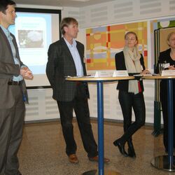 Vier Teilnehmer der Veranstaltung stehen um Bistrotische herum, bereit für eine Podiumsdiskussion 