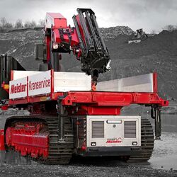 auf einem selbstfahrenden Raupenfahrzeug wird ein Kran durch bergiges Gelände und flaches Wasser transportiert