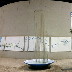 Kunstinstallation im Vorraum des UBA Dessau: über einer großen Schale hängt ein Vorhang aus Schnüren, an dem Wasser herunterläuft, man erkennt die Silhouette eines Menschen