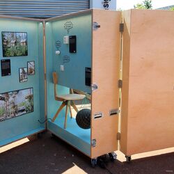 mannshohe Ausstellungsbox aus Holz auf Rollen, aufgeklappt sind Exponate zu sehen