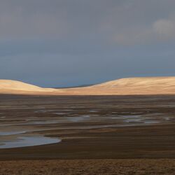 Arktische Landschaft: Die Sonne scheint auf einen Fluss und sanfte braune Hügel.