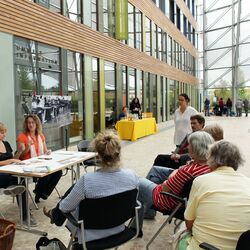 Gesprächsrunde zur Ausstellung: Zwei Frauen sitzen an einem Tisch, darum Publikum