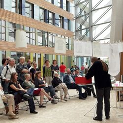 Kunstausstellung: Zwei Frauen stehen vor einer Wäscheleine und einem Bügelbrett und hängen Informationen für die Besucher an die Leine, davor Publikum