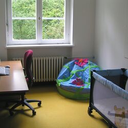 Eltern-Kind-Zimmer: gegenüber vom Schreibtisch steht ein Bett für Kleinkinder, in der Ecke liegt ein bunter Sitzsack