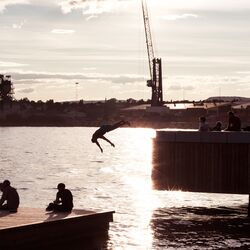 Im Hafen von Oslo: Bei untergehender Sonne springt ein Mann von einem Steg ins Wasser, davor sieht man zwei Personen, die in der Abendsonne sitzen.