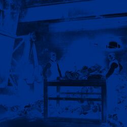 Zwei Arbeiter stehen zwischen einem Tisch, einem Berg Müll und einem Kran.