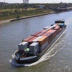Ein großes Containerschiff fährt bei Sonnenschein auf dem Rhein