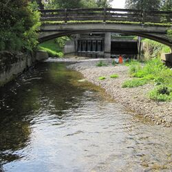 Flussansicht mit Brücke und im Hintergrund ist eine kleinere Stauanlage zu sehen