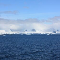 Eine weiße Wolkenschicht umgibt antarktische Berge an der Küste. Darüber sieht man eine zweite dunkler und dünnere Wolkenschicht. 