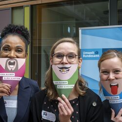 Kolleginnen mit Klimafächern vor dem Mund, mit lustigen Gesichtern. 