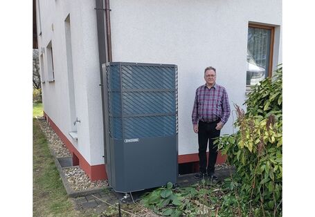 Ein Mann neben einer Wärmepumpe vor seinem Haus.