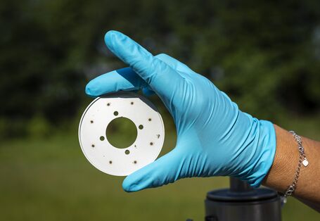 Das Bild zeigt die Hand einer Forschenden, die mit einem Laborhandschuh einen kleinen Messindikator hochhält. 