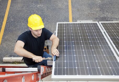 Ein Mann mit Bauhelm auf einer Leiter montiert eine Photovoltaikanlage