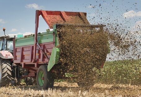 Ein Taktor mit Hänger verteilt Dünger auf einem Feld