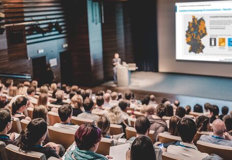 Foto eines vollbesetzten Hörsaals, an eine Leinwand wird eine Infografik zur umweltgerechten Entsorgung von Arzneimittelresten projiziert.