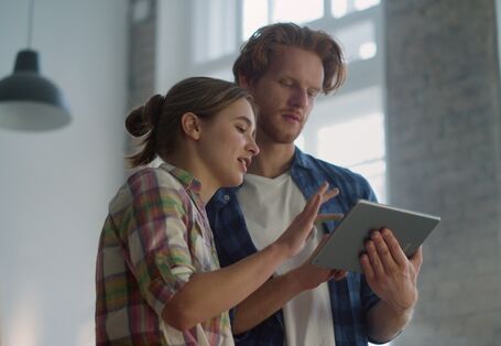 Eine Frau und ein Mann schauen auf ein Tablet. 