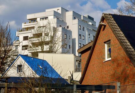 Einfamilienhäuser mit Photovoltaikanlagen auf dem Dach vor einem Plattenbau.