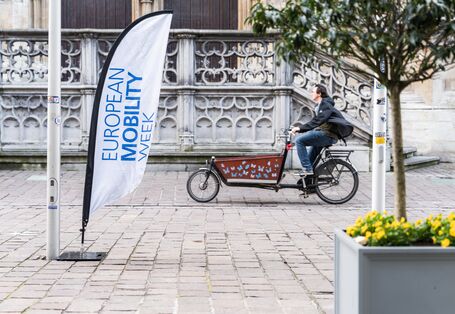 Ein Mann fährt auf einem Lastenrad an einem Banner mit der Aufschrift „European Mobility Week“ vorbei.