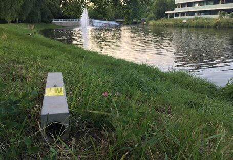 Köderstation mit Warnhinweis vor Rattengift steht am Uferbereich eines Flusses