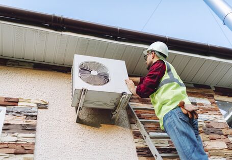 Ein Techniker steht auf einer Leiter und wartete eine Wärmepumpe.