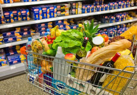 Voller Einkaufswagen vor Supermarktregal.