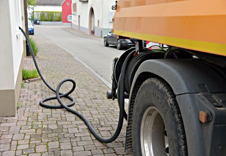 Ein Lastwagen steht am Straßenrand und pumpt über einen schwarzen Schlauch Öl in den Keller eines Hauses.