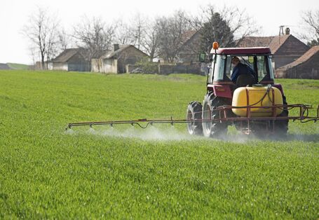 Ein Traktor fährt über ein grünes Feld und versprüht Pflanzenschutzmittel.