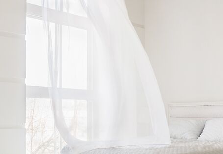 Lüften eines Schlafzimmers: der Vorhang weht über das Bett.