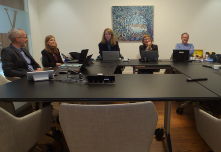 In a small meeting room, 7 people sit at a table.