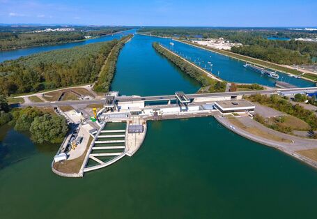 Foto: Das Wasserkraftwerk Iffezheim samt Staustufe am stark ausgebauten und begradigten Rhein. Im Vordergrund ist ein großer Fischpass zu sehen.