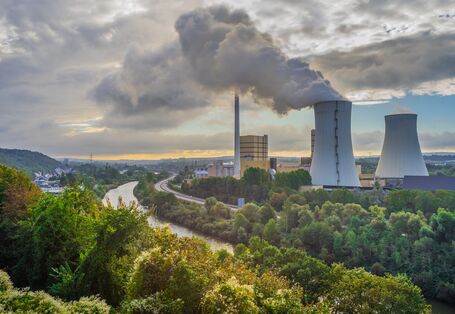 Foto: Zwei Kühltürme eines Wärmekraftwerks im unmittelbaren Umfeld eines Flusses. Aus einem Kühlturm tritt Wasserdampf aus.