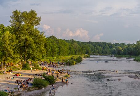 Foto: Ein renaturierter Abschnitt der Isar bei München mit zahlreichen Badegästen am Kiesstrand und im Wasser.