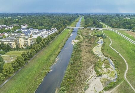 Luftbild der renaturierten Murg. Im Vordergrund liegt ein geschwungenes Nebengewässer mit Kiesbänken, Laufweitungen und Verengungen. Im Hintergrund liegt der reaktivierte Auwald.