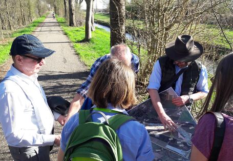 Foto: Mehrere Personen blicken vor einem technisch ausgebauten Fluss auf Planungsunterlagen.