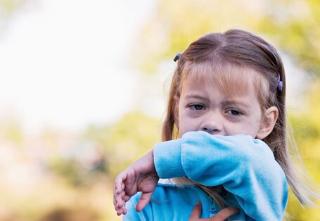 Ein Kind hustet in seinen Ärmel