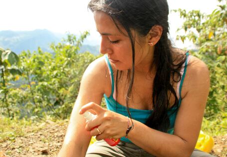 Eine Frau sprüht sich mit Mückenschutzspray ein