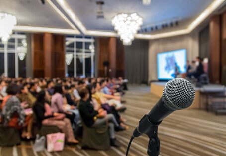Mikrofon in einem Ständer, im Hintergrund ein Saal mit Zuhörern