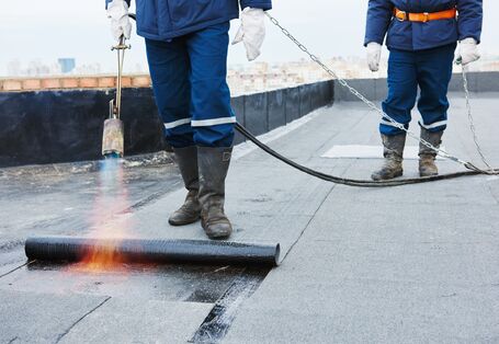 Bauarbeiter verlegen bitumenhaltige Dachbahnen.