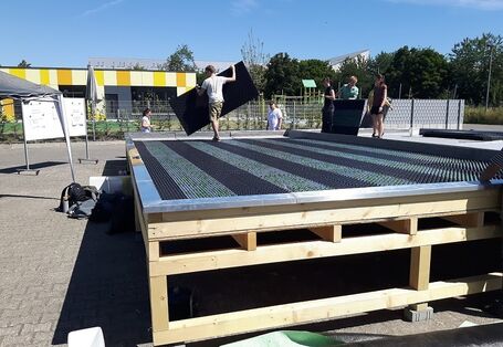 Studierende verlegen Bodenplatten auf einem Holzgerüst.