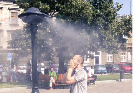 Ein Mann steht vor einem Sprühvernebeler und im Hintergrund sitzen Menschen unter einem Baum