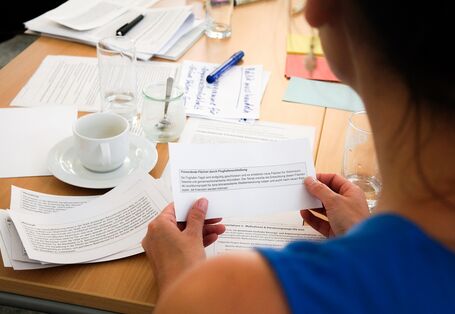 Eine Frau sitzt an einem Gruppentisch und hält eine Zettelstück