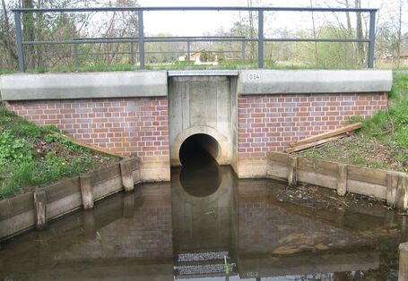 Auf dem Foto ist die Verrohrung eines Bachs unter einer Brücke dargestellt