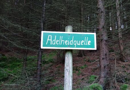 Auf dem Bild ist ein Schild mit der Aufschrift Adelheidquelle dargestellt