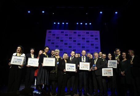 Alle Finalistinnen und Finalisten stehen gemeinsam auf der Bühne und die Preisträgerkommunen zeigen ihre Preise