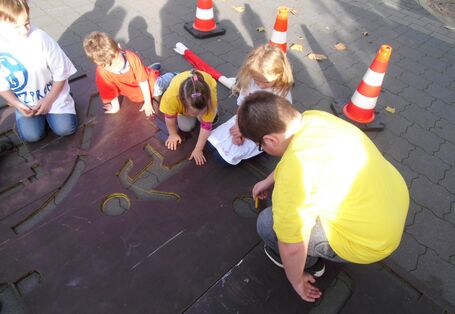 Kinder zeichnen die Umrisse des Verkehrsschilds auf den Boden