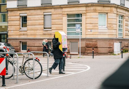 Person läuft mit umgedrehten Periskop über die Straße an einer Stuttgarter Ecke.